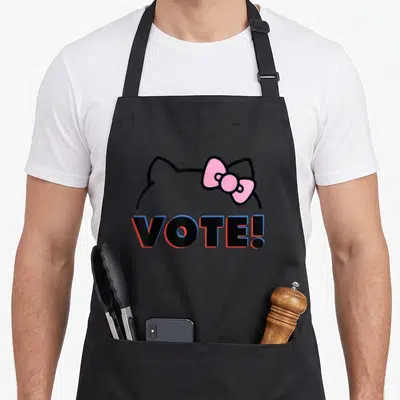 Vote bow apron - Hello Kitty head outline with pink bow above VOTE! text in black blue red white — shown on a black cotton canvas apron against a white background