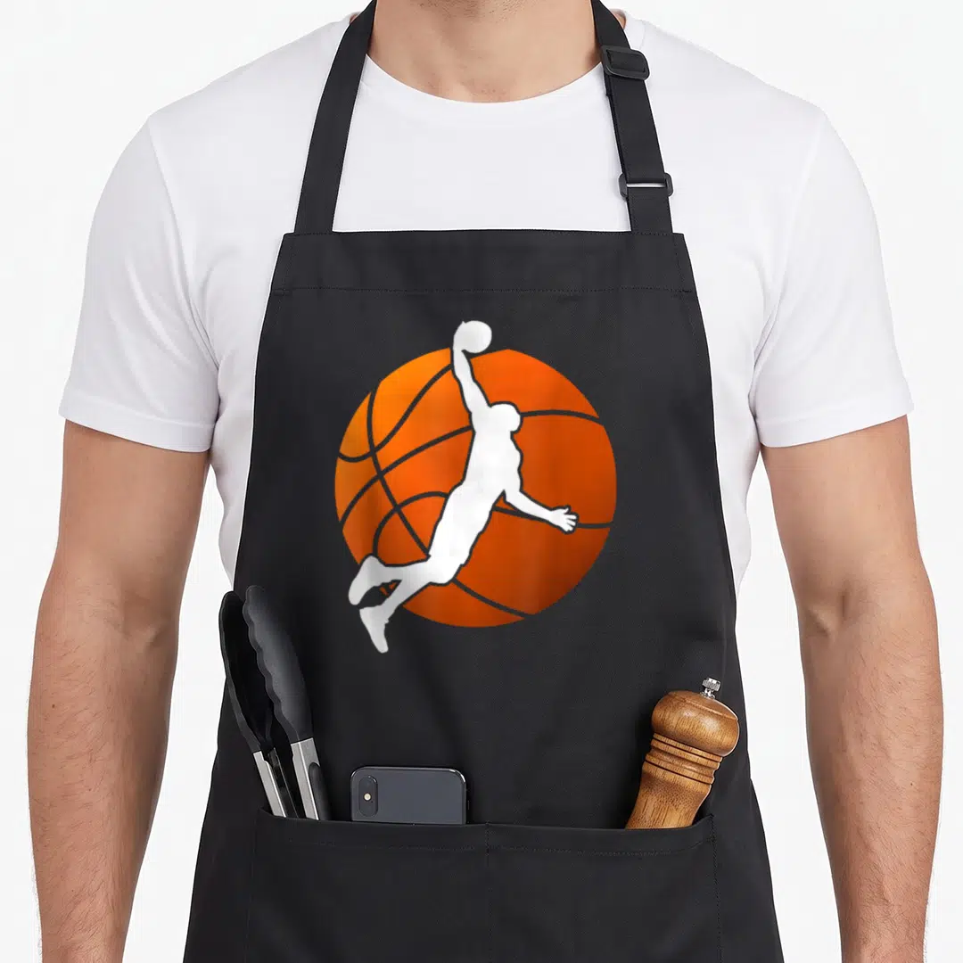 Basketball throw player apron - White basketball player silhouette jumping in front of an orange ball — shown on a black cotton canvas apron against a white background