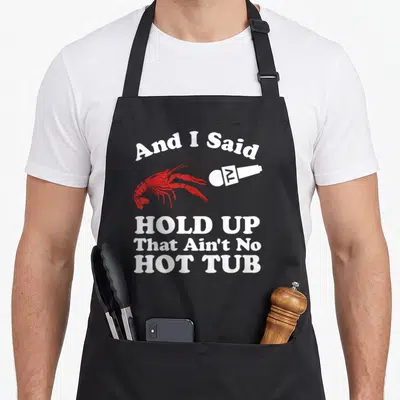 Hot cajun aprons - Red lobster facing white microphone with arched text And I Said Hold Up That Ain't No Hot Tub — shown on a black cotton canvas apron against a white background