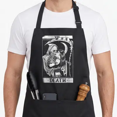 Blackcraft tarot card apron - White line art of skeleton kissing woman with scythe and moon, labeled XIII DEATH — shown on a black cotton canvas apron against a white background