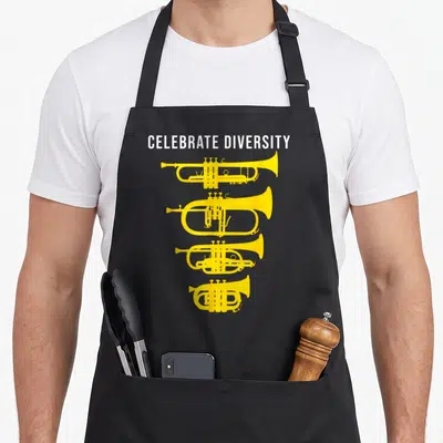 Trumpet celebrate diversity apron - Four yellow brass instruments stacked vertically under white CELEBRATE DIVERSITY — shown on a black cotton canvas apron against a white background