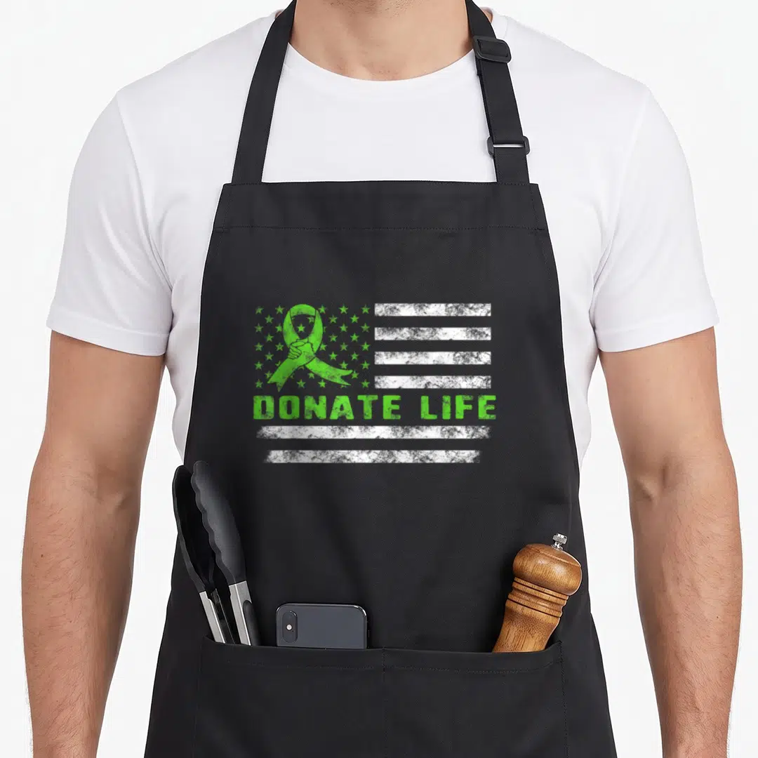 Flag donate organ apron - Distressed green ribbon and white stripes with DONATE LIFE text on a flag background — shown on a black cotton canvas apron against a white background
