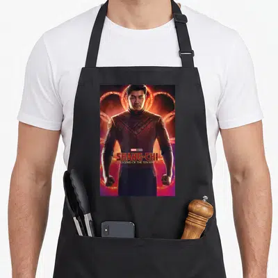 Shang chi apron - Man in red armor with glowing rings and Shang-Chi Legend of the Ten Rings title text — shown on a black cotton canvas apron against a white background