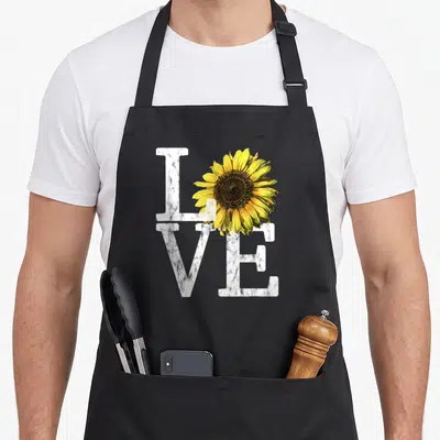 Sunflower white nurse apron - Marble-textured LOVE text with a realistic yellow and brown sunflower overlapping — shown on a black cotton canvas apron against a white background