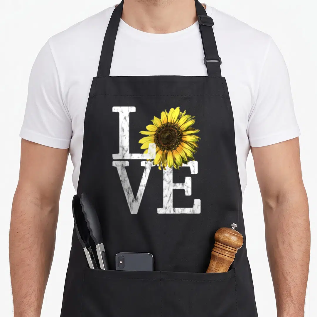 Sunflower white nurse apron - Marble-textured LOVE text with a realistic yellow and brown sunflower overlapping — shown on a black cotton canvas apron against a white background
