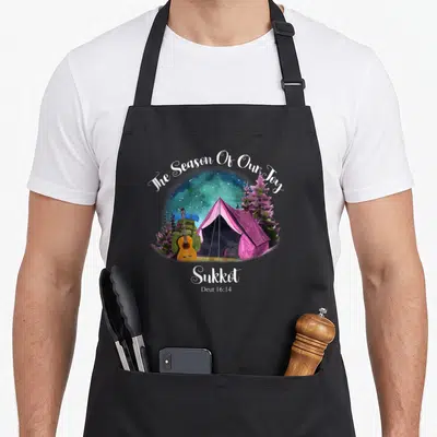 Sukkot dressedforduty apron - Pink tent camping scene with guitar and trees under starry sky with The Season Of Our Joy — shown on a black cotton canvas apron against a white background