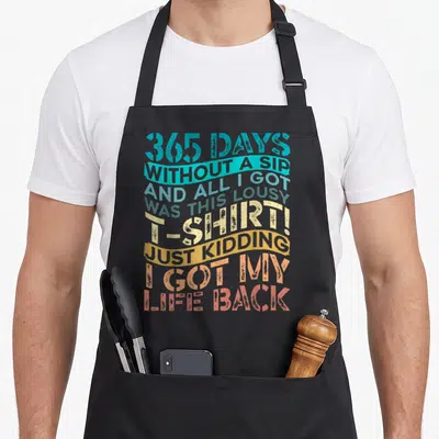 Sober alcohol recovery apron - Stacked colorful typography reading 365 days without a sip and all I got was this lousy — shown on a black cotton canvas apron against a white background