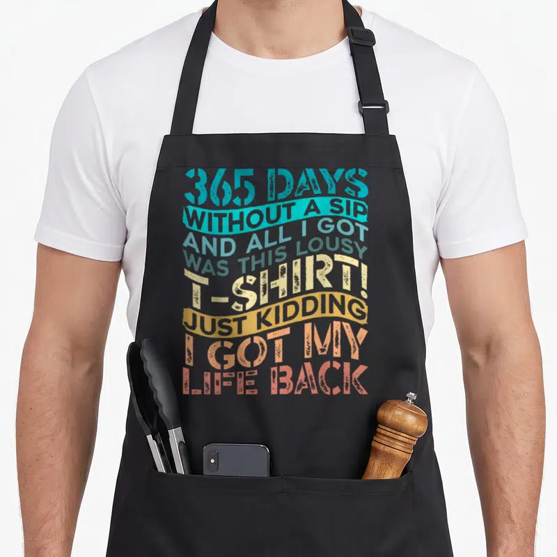Sober alcohol recovery apron - Stacked colorful typography reading 365 days without a sip and all I got was this lousy — shown on a black cotton canvas apron against a white background