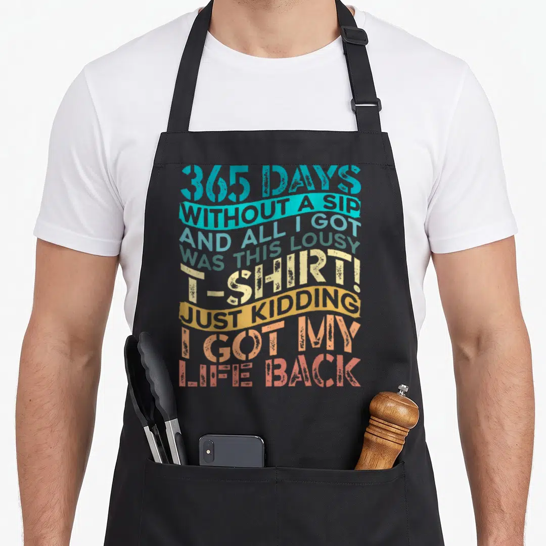Sober alcohol recovery apron - Stacked colorful typography reading 365 days without a sip and all I got was this lousy — shown on a black cotton canvas apron against a white background