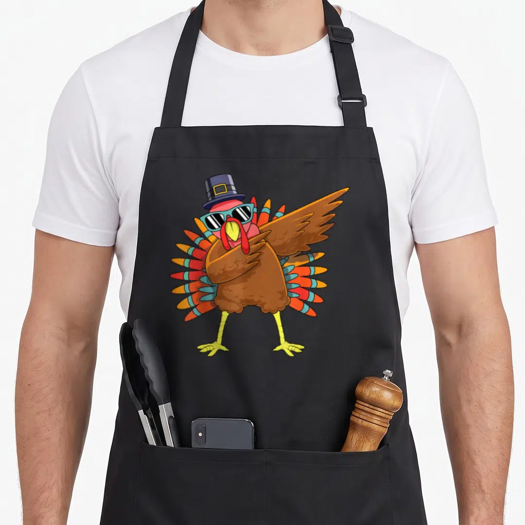 Dab pilgrim apron - Cartoon brown turkey wearing blue hat and sunglasses in a dab pose — shown on a black cotton canvas apron against a white background