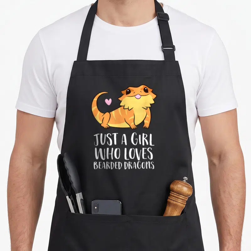 Reptile dragon apron - Cartoon orange bearded dragon with pink heart and white text — shown on a black cotton canvas apron against a white background