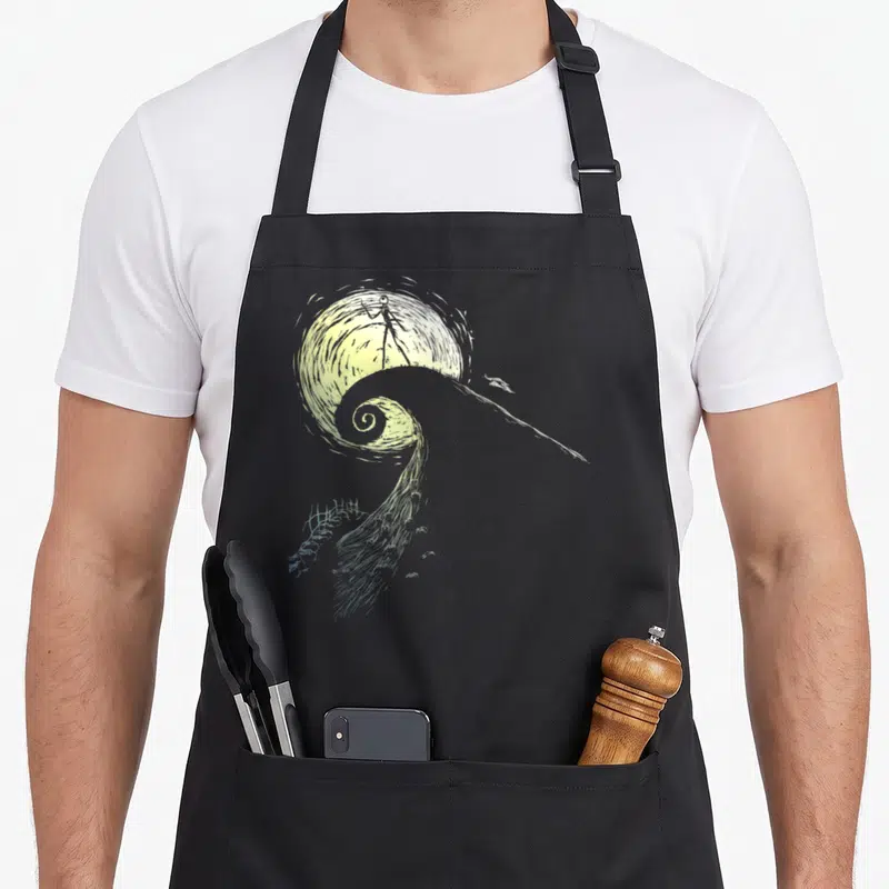 Spiral jack apron - Line art of Jack Skellington on spiral hill against moon in yellow grey white — shown on a black cotton canvas apron against a white background