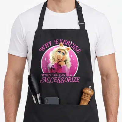 Piggy little miss apron - Miss Piggy in pink circle with text WHY EXERCISE WHEN YOU CAN ACCESSORIZE — shown on a black cotton canvas apron against a white background
