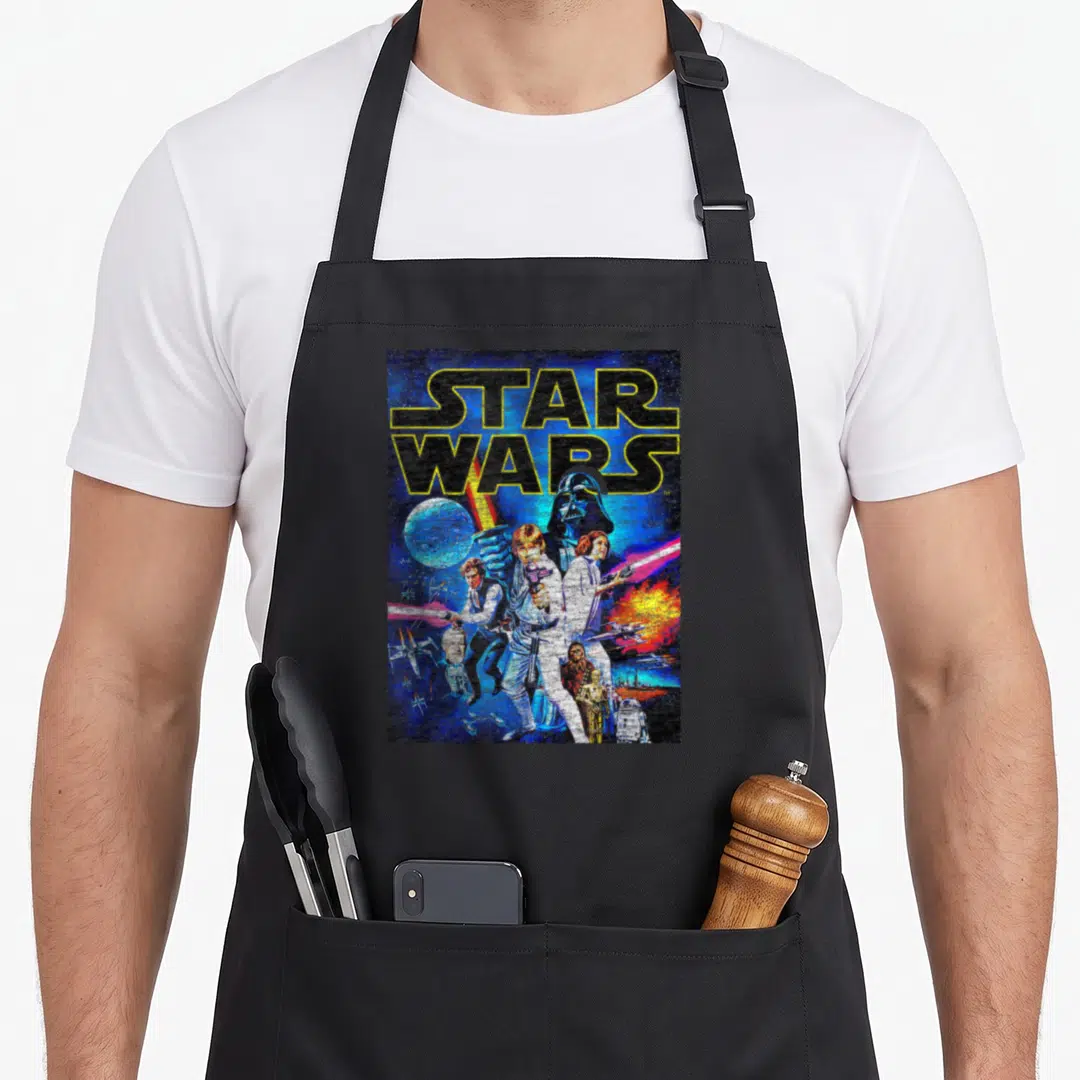 Movie new hope apron - Retro star wars poster with Darth Vader, Death Star, characters, and space battles in yellow — shown on a black cotton canvas apron against a white background