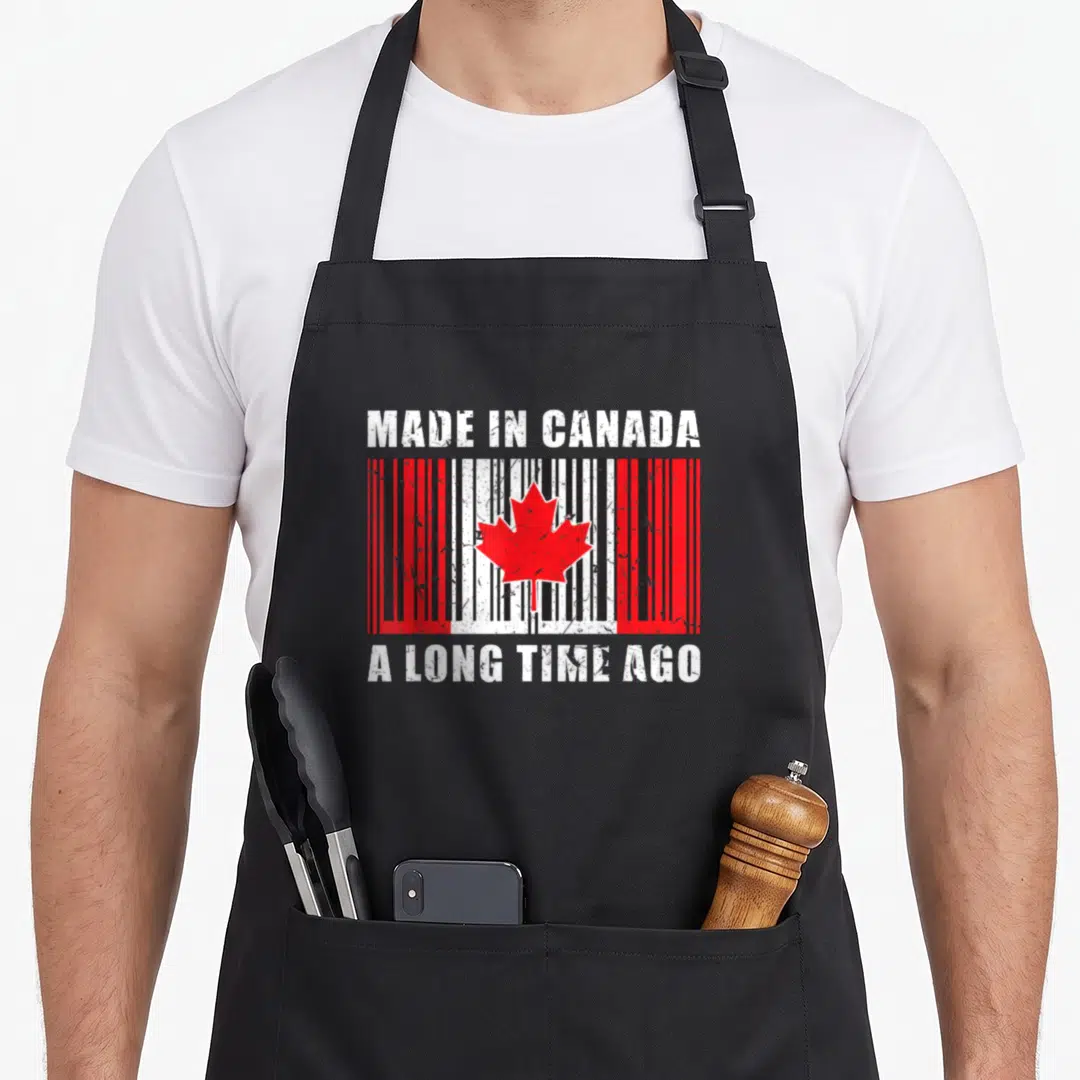 Ago canadian made aprons - Distressed barcode with red maple leaf and stacked text Made In Canada A Long Time Ago — shown on a black cotton canvas apron against a white background
