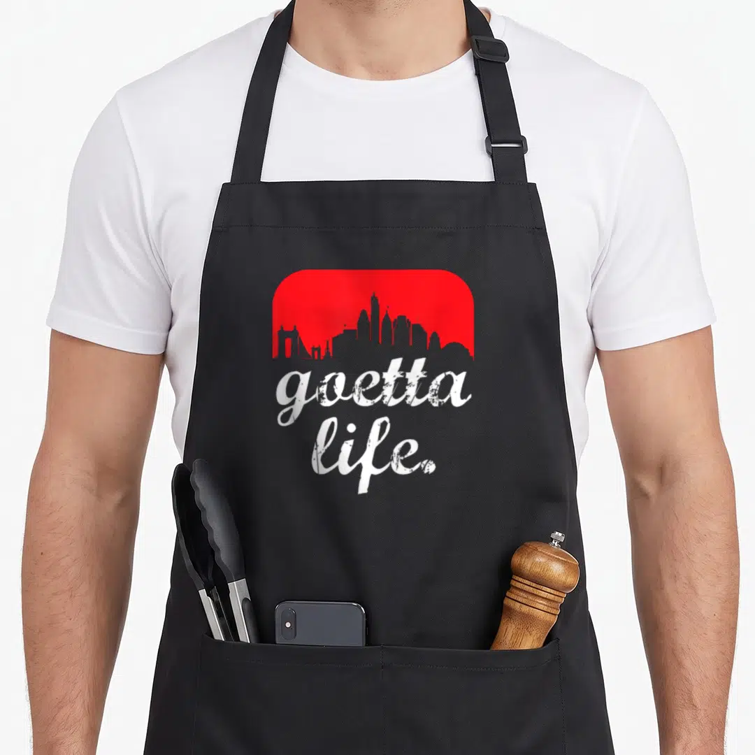 Goetta food aprons - Red rounded rectangle with grey skyline silhouette and white goetta life text — shown on a black cotton canvas apron against a white background