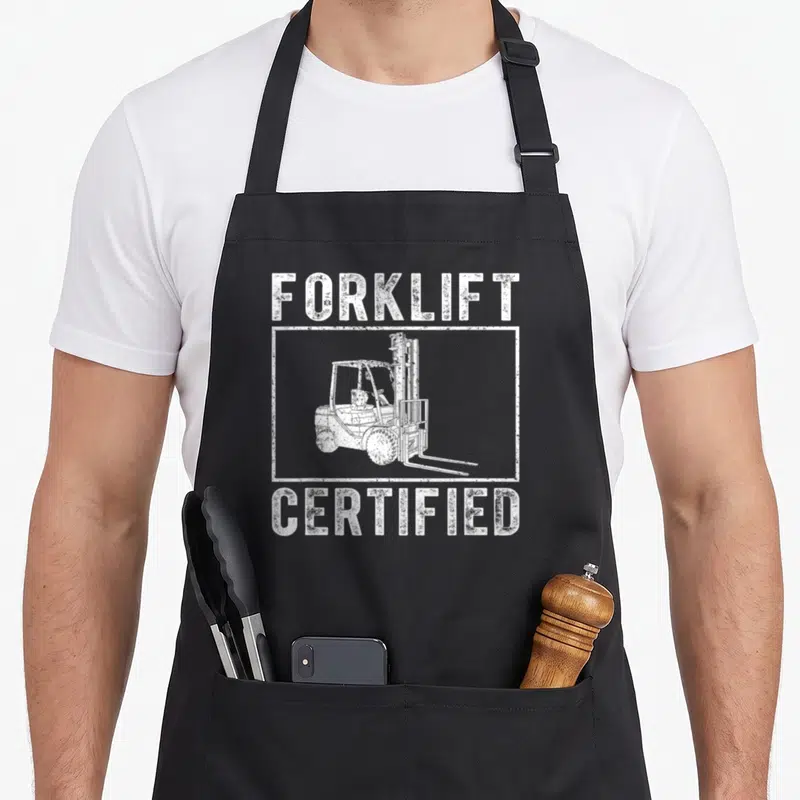 Certified forklift humor apron - White distressed text Forklift Certified with forklift illustration in rectangular — shown on a black cotton canvas apron against a white background