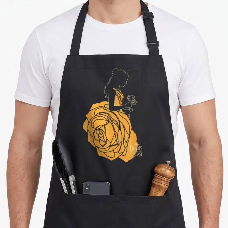Beast rose apron - Woman silhouette in yellow rose dress holding flower with Beauty and the Beast text — shown on a black cotton canvas apron against a white background