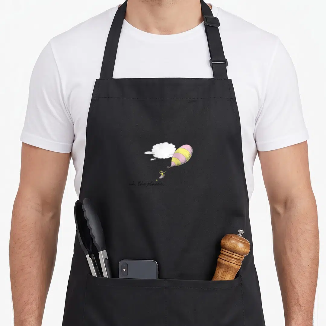Youll balloon apron - Striped pink and yellow balloon with person in basket and oh the places text below — shown on a black cotton canvas apron against a white background