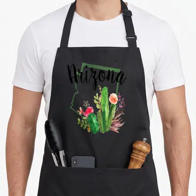 State cactus apron - Arizona text over green state outline with watercolor cacti and pink orange flowers — shown on a black cotton canvas apron against a white background