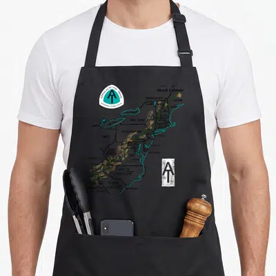 Appalachian markers apron - Map of Eastern US listing states like PA and NC with green trail line and logos — shown on a black cotton canvas apron against a white background