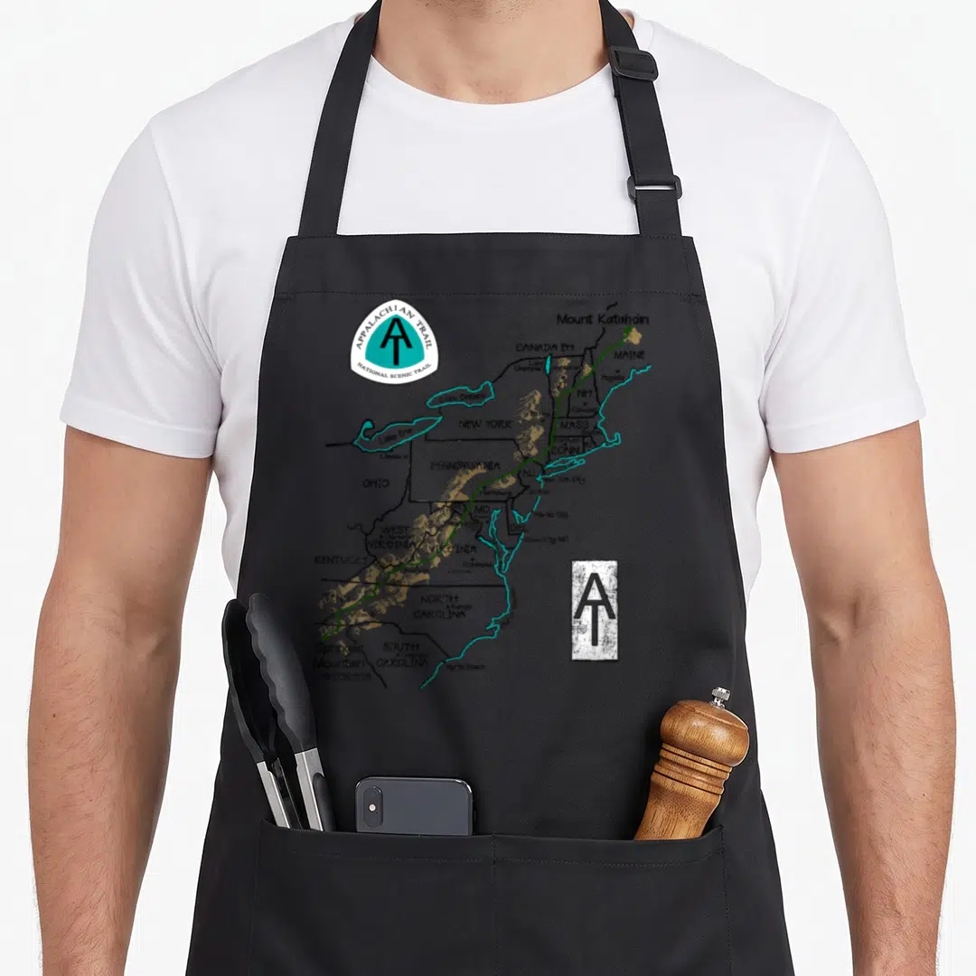 Appalachian markers apron - Map of Eastern US listing states like PA and NC with green trail line and logos — shown on a black cotton canvas apron against a white background