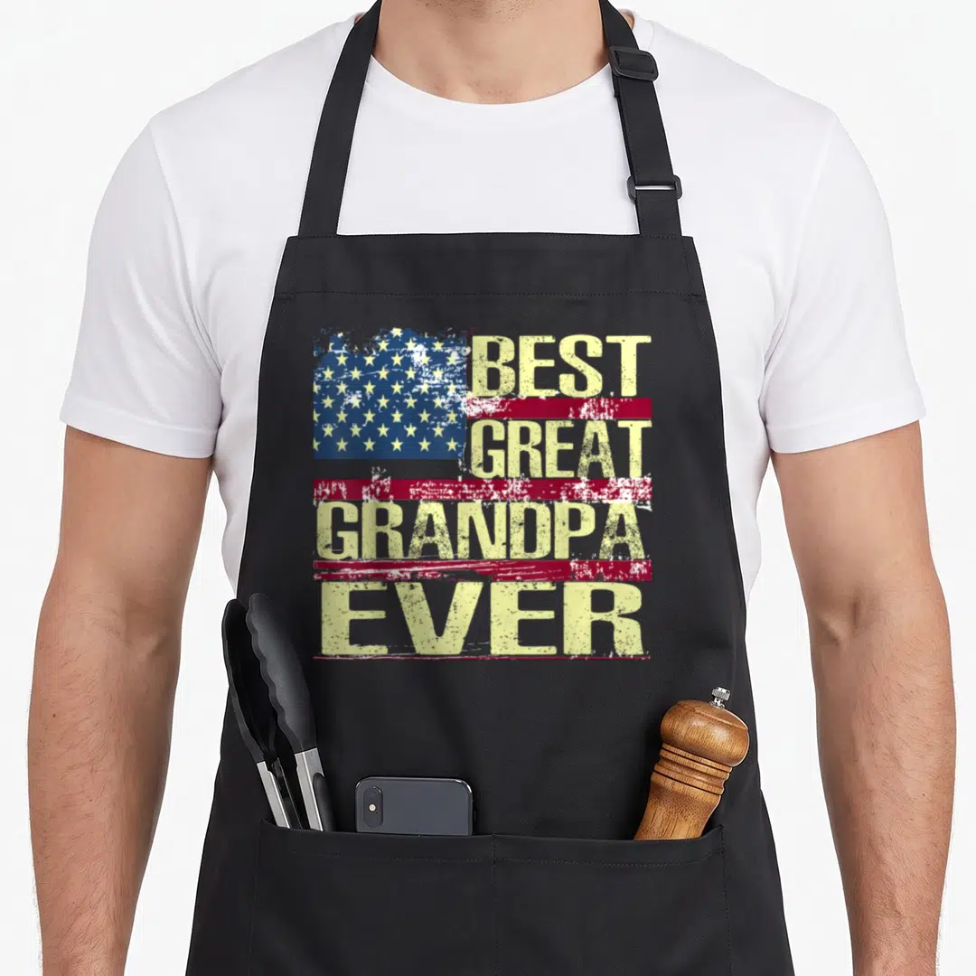 Funny grandpa american flag apron - Distressed yellow text reading Best Great Grandpa Ever over red stripes and blue — shown on a black cotton canvas apron against a white background