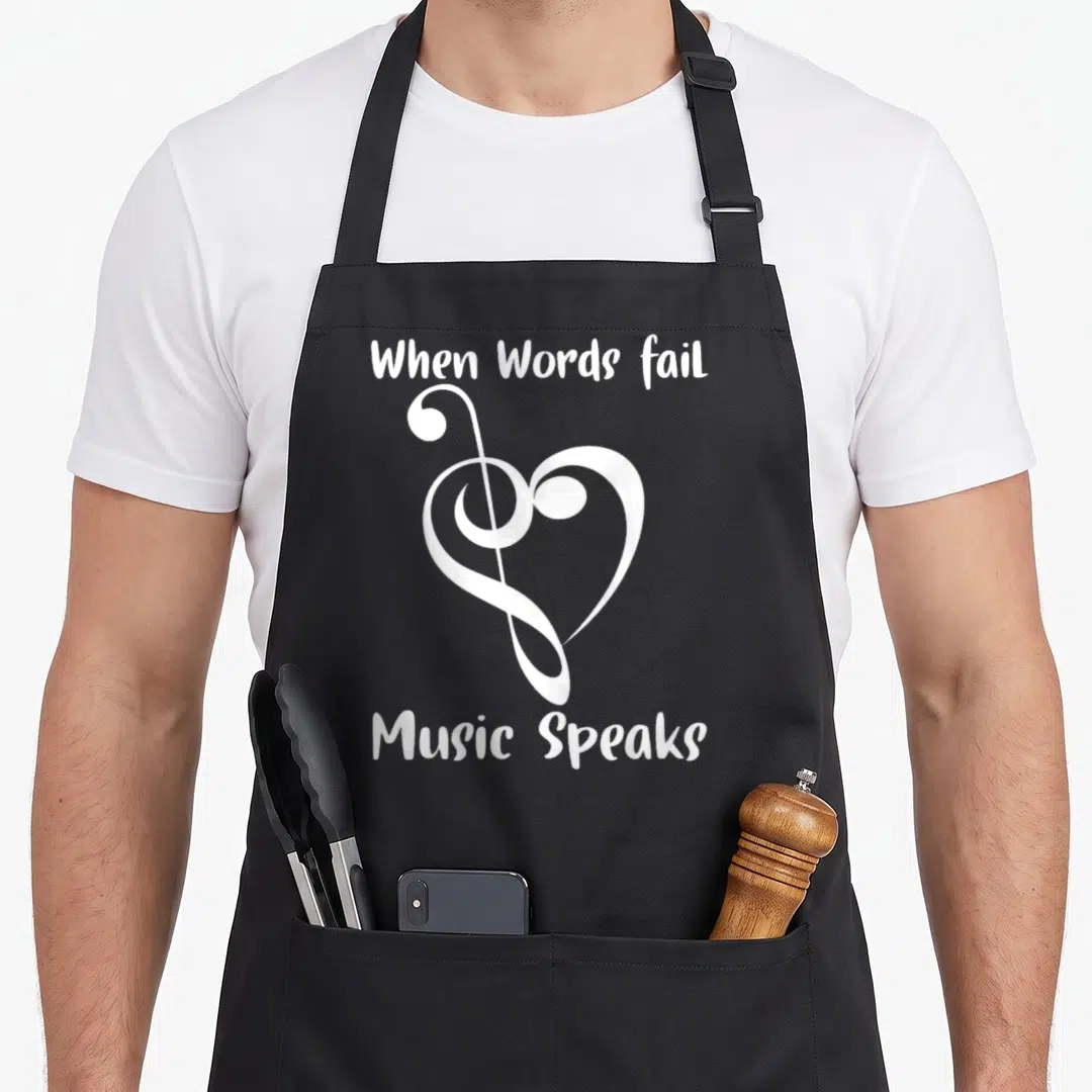 Musical music quotes apron - White treble clef shaped like a heart with text When Words fail Music Speaks — shown on a black cotton canvas apron against a white background