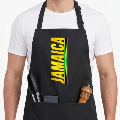 Funny flag jamaican apron - Vertical yellow JAMAICA text beside narrow green black and yellow rectangular flag design — shown on a black cotton canvas apron against a white background