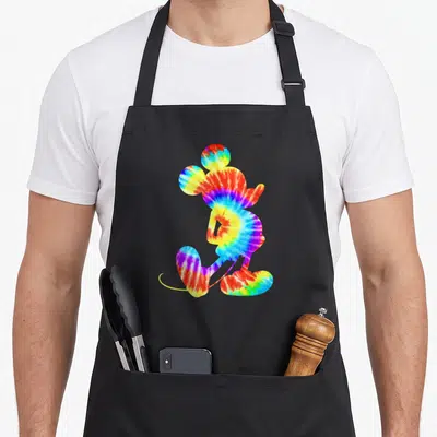 Dye tie apron - Mickey Mouse silhouette filled with red yellow green blue purple tie-dye pattern — shown on a black cotton canvas apron against a white background