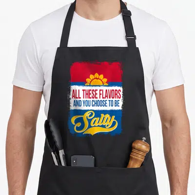 These sunflower apron - Yellow sun on red and blue background with text ALL THESE FLAVORS AND YOU CHOOSE TO BE Salty — shown on a black cotton canvas apron against a white background
