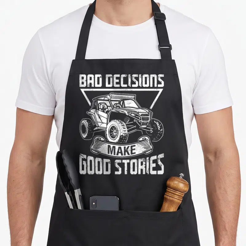 Sxs vehicle apron - Distressed white BAD DECISIONS MAKE GOOD STORIES text with UTV in triangle frame on black apron — shown on a black cotton canvas apron against a white background