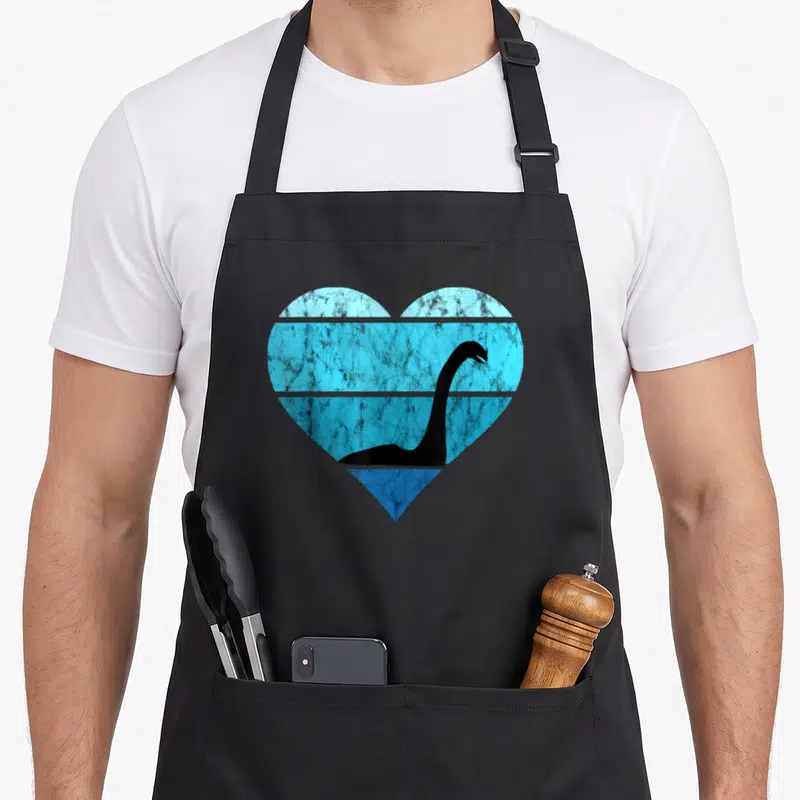 Ocean loch ness monster apron - Black dinosaur silhouette inside a heart with four distressed blue horizontal bands — shown on a black cotton canvas apron against a white background