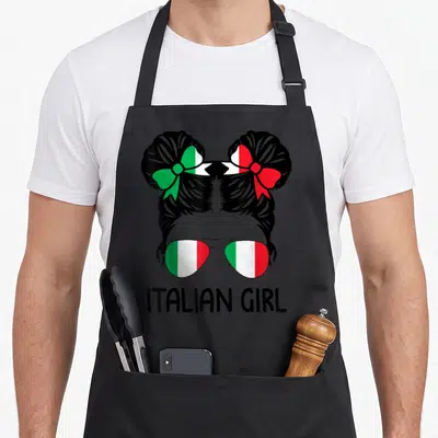 Messy italian aprons - Cartoon girl silhouette with flag buns and sunglasses above ITALIAN GIRL text — shown on a black cotton canvas apron against a white background