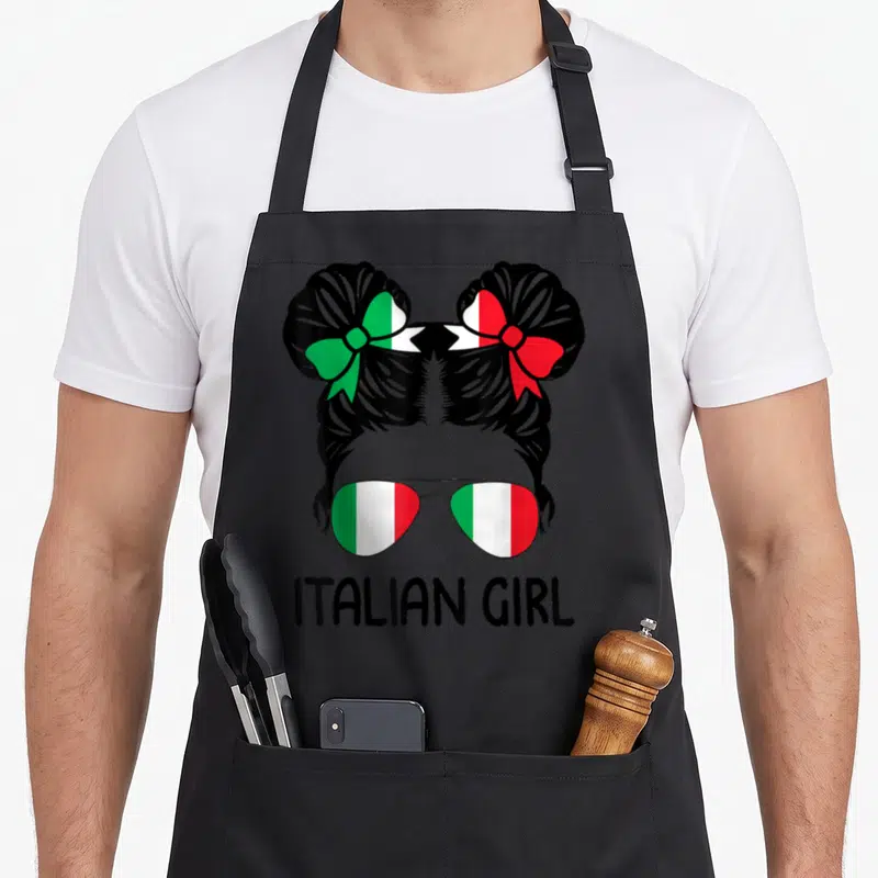 Messy italian aprons - Cartoon girl silhouette with flag buns and sunglasses above ITALIAN GIRL text — shown on a black cotton canvas apron against a white background
