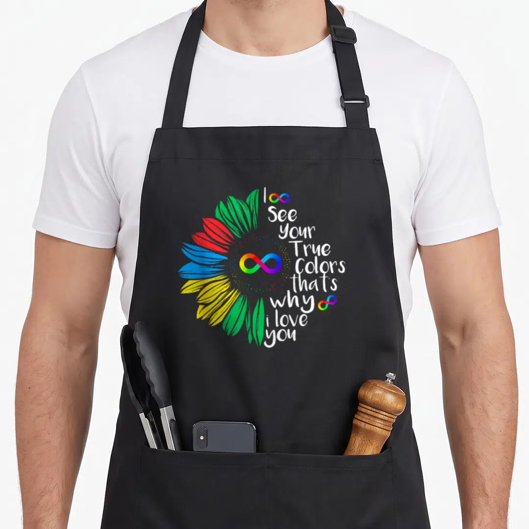 See rainbow apron - Rainbow flower with I See Your True Colors text and infinity symbols — shown on a black cotton canvas apron against a white background