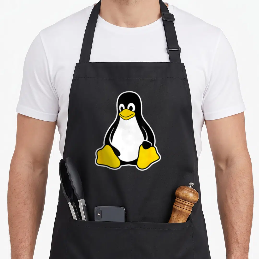 Tux penguin aprons - Cartoon penguin with black back, white belly, and yellow feet surrounded by white border — shown on a black cotton canvas apron against a white background