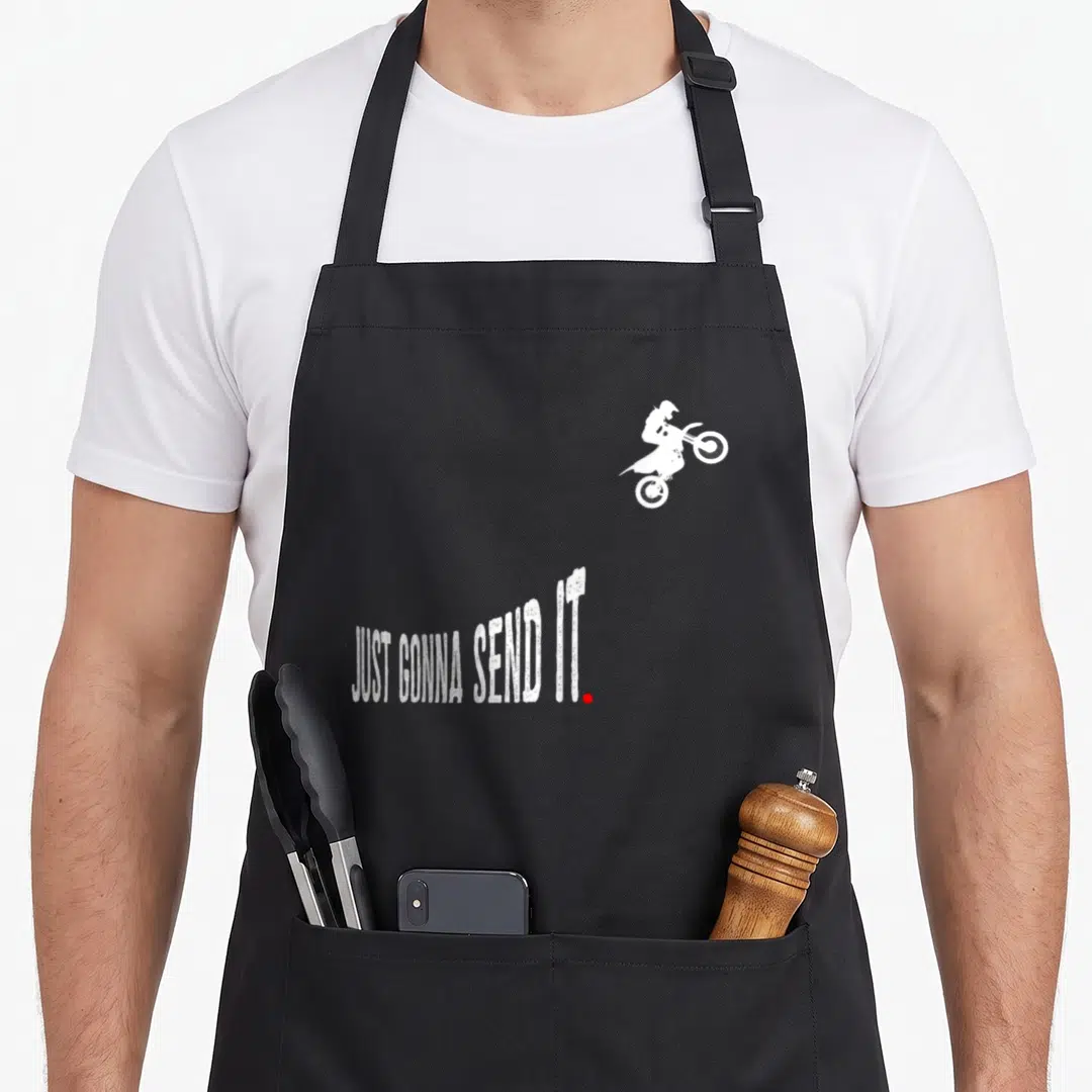 Send bike apron - Distressed white Just Gonna Send It text curving under a motocross rider silhouette with a red dot — shown on a black cotton canvas apron against a white background