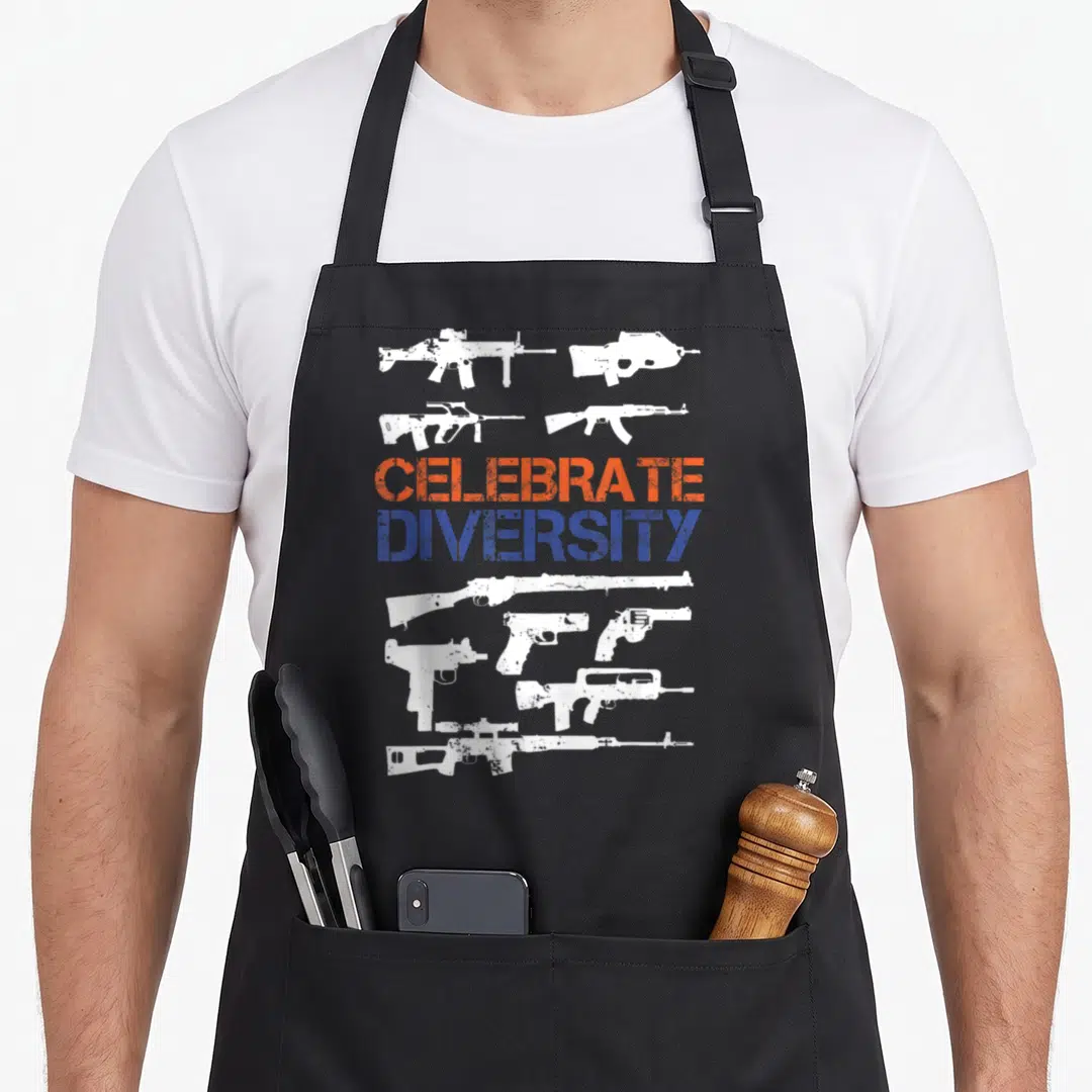 Diversity gun apron - Nine distressed white guns surrounding orange and blue CELEBRATE DIVERSITY text on black bib apron — shown on a black cotton canvas apron against a white background