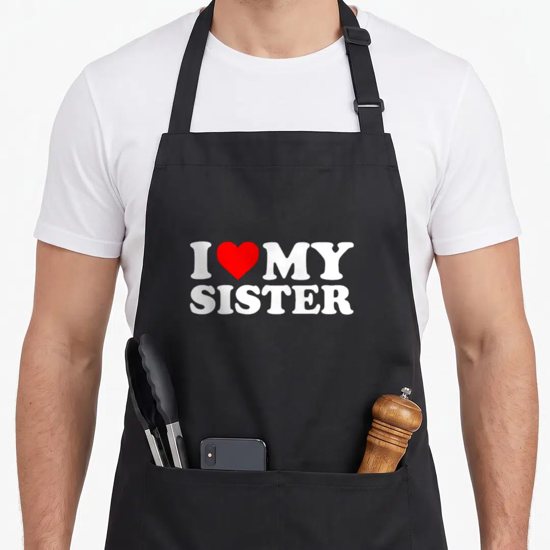 Cute sister nun apron - White I MY SISTER text with red heart on black apron — shown on a black cotton canvas apron against a white background