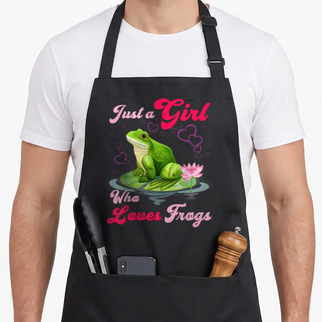 Cool frog aprons - Green frog on lily pad with pink lotus and hearts. Text Just a Girl Who Loves Frogs in pink script — shown on a black cotton canvas apron against a white background