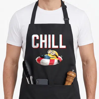 Chillaxin bobsled apron - Yellow minion floating in red and white tube below white CHILL text — shown on a black cotton canvas apron against a white background