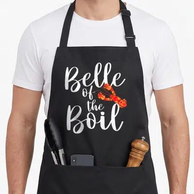 Belle crawfish boil apron - Geometric red and orange lobster overlapping stacked white text reading Belle of the Boil — shown on a black cotton canvas apron against a white background