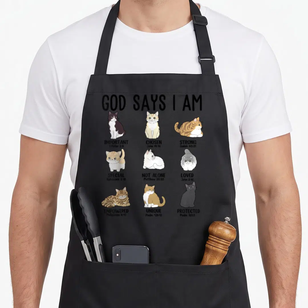 Cat god says i am apron - Nine cartoon cats in a grid with affirmations like Important and Chosen alongside Bible verses — shown on a black cotton canvas apron against a white background