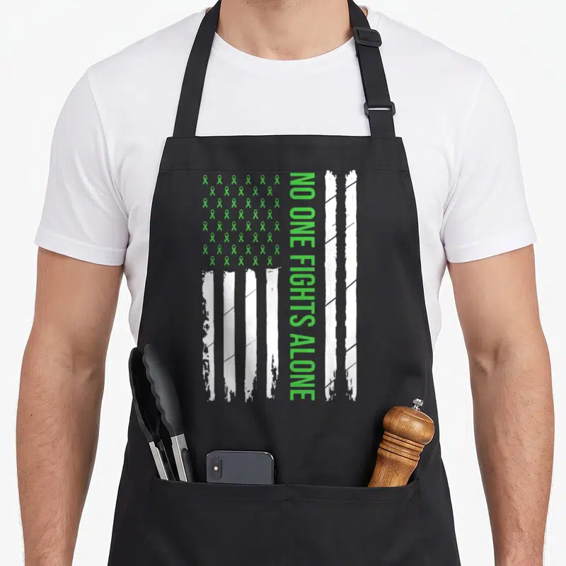 Mental ribbon apron - Distressed green ribbon grid and white stripes with vertical NO ONE FIGHTS ALONE text — shown on a black cotton canvas apron against a white background