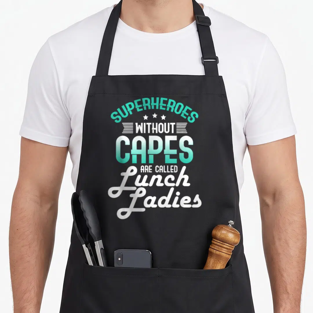 Cape lunch lady apron - SUPERHEROES WITHOUT CAPES ARE CALLED Lunch Ladies text with three stars and horizontal lines — shown on a black cotton canvas apron against a white background