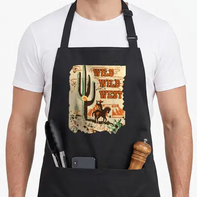 Wild western apron - Retro cactus and cowboy on horseback with stacked Wild Wild West text on torn paper — shown on a black cotton canvas apron against a white background
