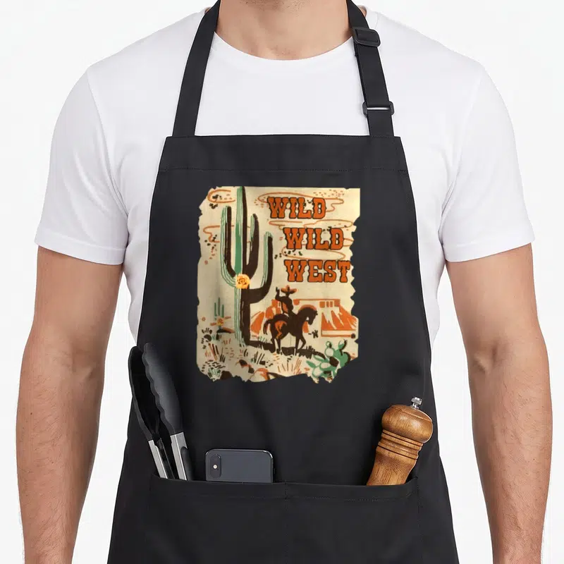 Wild western apron - Retro cactus and cowboy on horseback with stacked Wild Wild West text on torn paper — shown on a black cotton canvas apron against a white background
