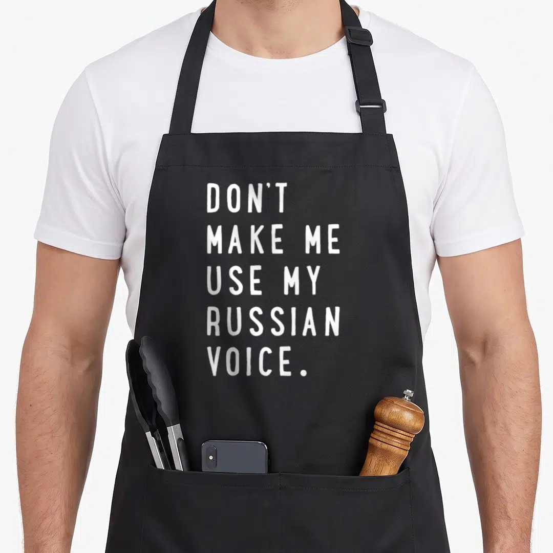 Use russian apron - White text reading DON'T MAKE ME USE MY RUSSIAN VOICE stacked vertically — shown on a black cotton canvas apron against a white background