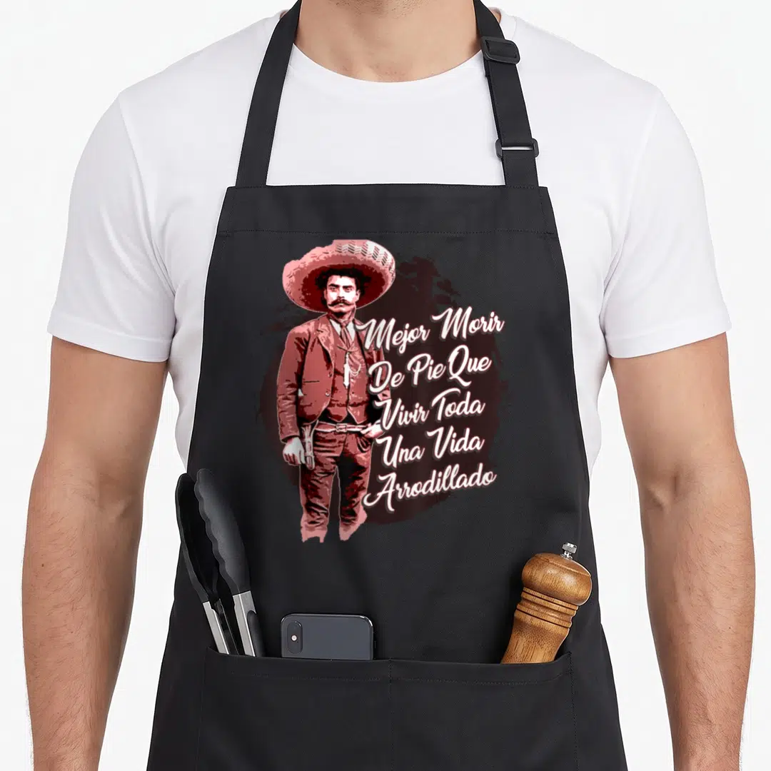 Emiliano mexican apron - Standing man in sombrero beside stacked Spanish text 'Mejor Morir De Pie' on dark splatter — shown on a black cotton canvas apron against a white background